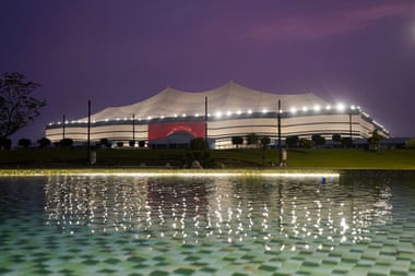A tent-like stadium at dusk seen from an ornamental pool