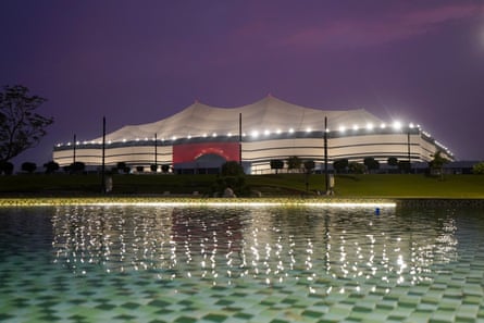 A tent-like stadium at dusk seen from across an ornamental pool