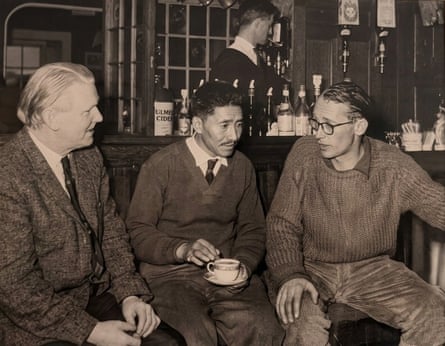 Three men sit in front of a wood-panelled bar, Tenzing with a cup and saucer in his lap