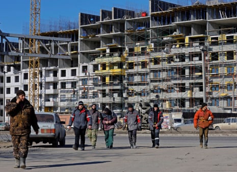 Los trabajadores caminan frente a un edificio de apartamentos en construcción en la ocupada Mariupol.