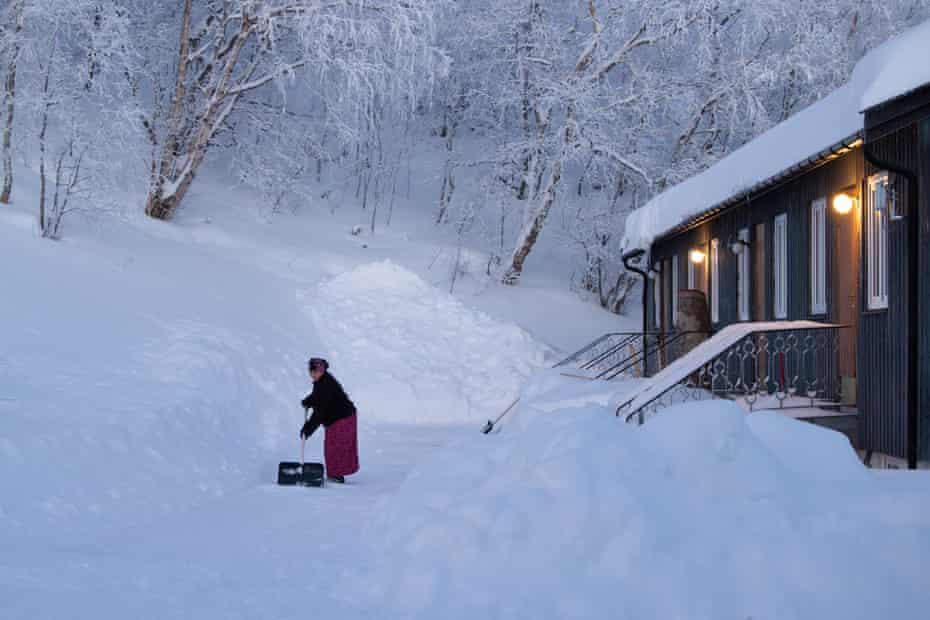 A woman shovels snow outside a log cabin