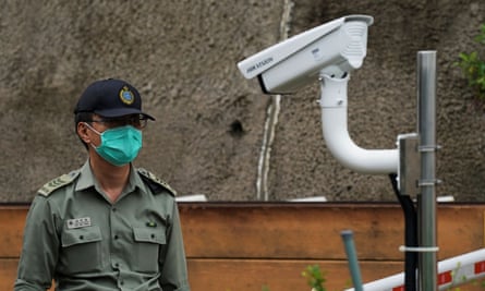 A police officer stands near a Hikvision camera at a prison entrance in Hong Kong.