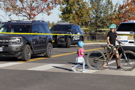 A mother and daughter cross a street past police cars and tape near a school