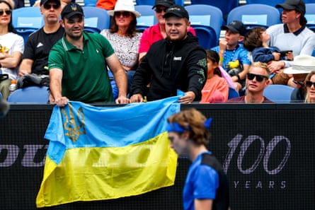 Two spectators hold a Ukrainian flag next to Andrey Rublev of Russia during his second round match against Emil Ruusuvuori