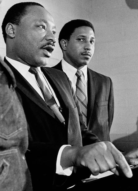 Two Black men in suits, one speaking and gesturing at a lectern.