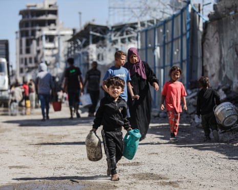 Palestinians carry water-filled canisters between collapsed houses as Palestinians, including children, fill bottles with water from water tanks brought in by trucks to meet their need for clean water at Tel al-Hawa neighbourhood of Gaza City, Gaza on 16 October 2025.