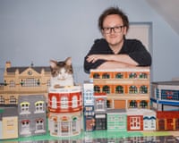 Chris Burton leans beside his cat Henry, leaning on his detailed Lego model buildings