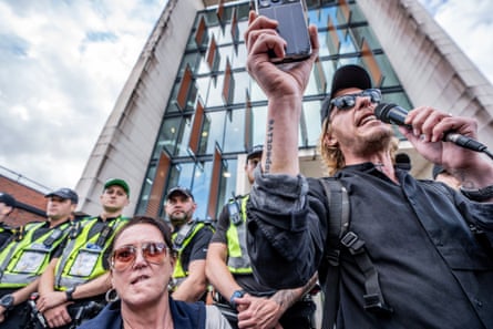 Lawrence Fox speaks into a microphone while police stand in the background