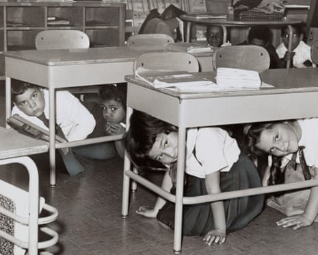 Children crouch under school desks during a drill in a classroom. Students at a Brooklyn middle school have a 'duck and cover' practice drill in preparation for a nuclear attack; silver print, 1962.