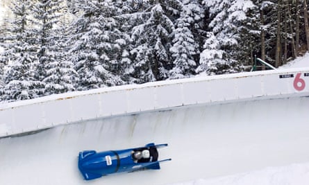A blue bobsleigh on a run with snowy trees in the background