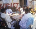 Four African-American senior citizens sit outdoors around a table, playing cards together