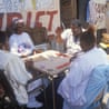 Four African-American senior citizens sit outdoors around a table, playing cards together