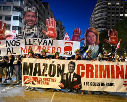 Demonstrators hold banners depicting Carlos Mazón and Susana Camarero with large bloodied hands and a placard reading 'Mazón - criminal'