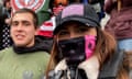 Two men and one woman in a row smiling for a selfie. Woman wears black hat with American flag, black and pink mask obscuring her face, black flak jacket and black leather jacket.
