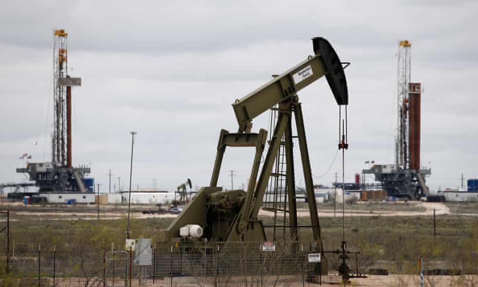Two oil drilling rigs seen in background behind a pump jack in an oil field near Midland, Texas.