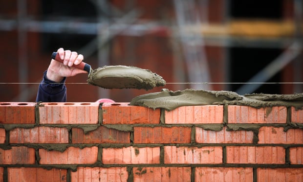 A construction worker holds a trowel of cement as he lays bricks at a construction site