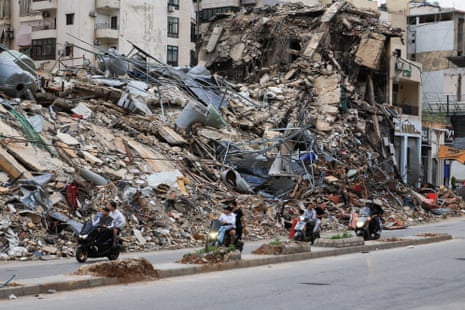 Four motorbikes ride past a building destroyed in an airstrike.