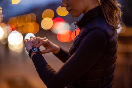 Woman using a fitness app on her smartwatch. She is outdoors in the city at night for a run.