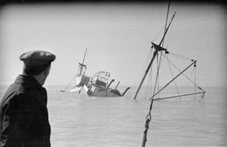A man in a cap watches a ship sinking.