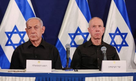 Netanyahu (left) and Gallant sitting side by side at a table with microphones, with Israeli flags in the background