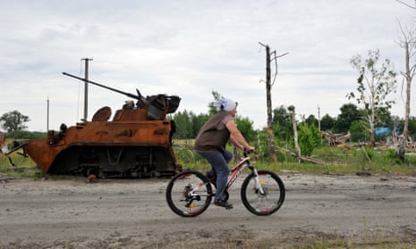 A woman rides bicycle past remains of a destroyed Russian armoured personnel carrier in the village of Teterivske, Kyiv region.