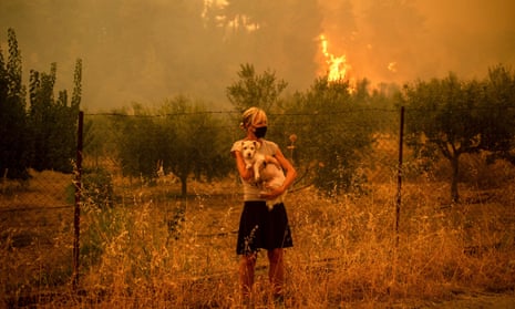 A woman holds a dog in her arms as forest fires approach the village of Pefki on Evvia, Greece's second largest island, in August as the region suffered its worst heatwave in decades, which experts have linked to climate change.