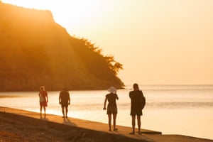 Four people walk along the coastline at sunset