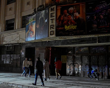 People walk past a closed cinema as shops close early under a government-ordered curfew in Cairo, Egypt.