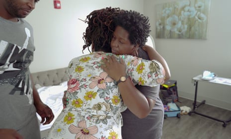 Two women hug each other as a man looks on nearby.