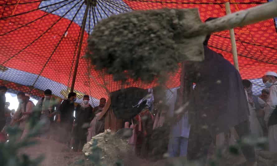 A shovel of dirt is thrown on a grave in Kabul, as Hazara men stand in the background