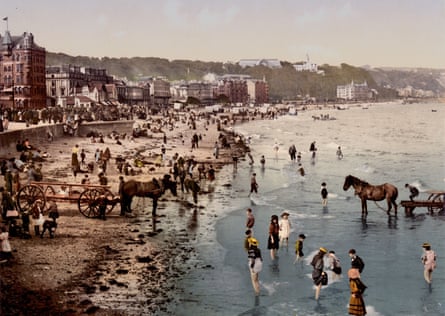 People in 19th century clothing on beach with horses and town seafront