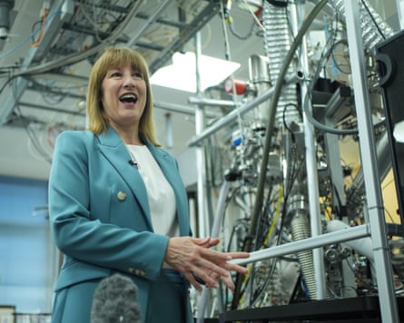 Rachel Reeves in a laboratory at Imperial College with equipment behind her; she is speaking to the press and wears a pale turquoise suit.