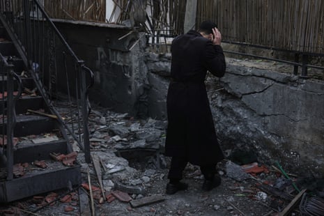 A man dressed in black clutches his head and faces away from the camera while standing in the blackened debris of a building damaged by a rocket fired from Lebanon.