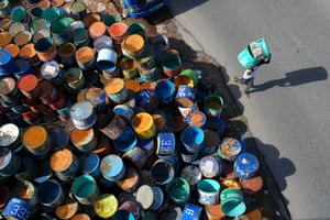A pile of brightly coloured half-oil drums from which a man is carrying two on his shoulder