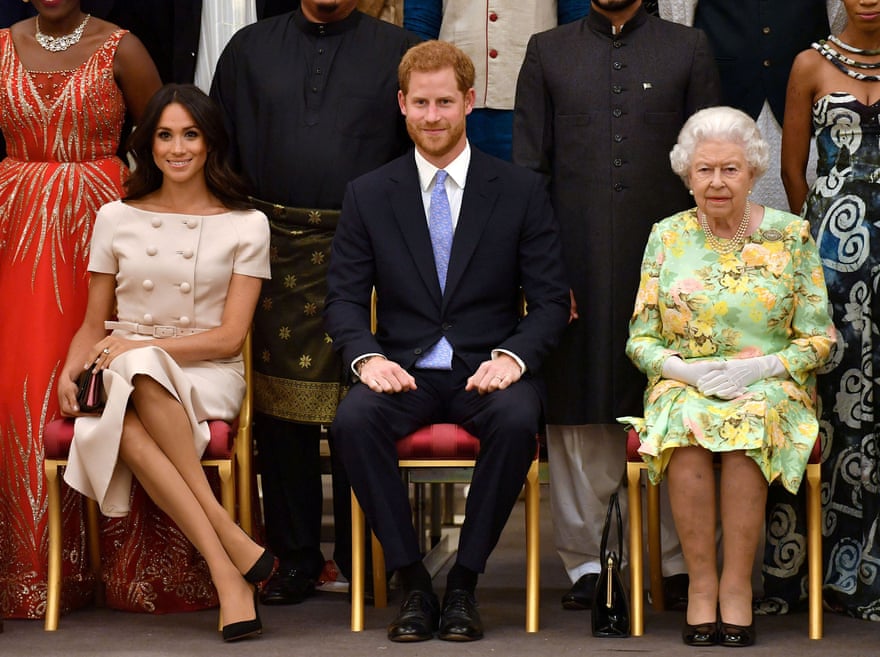 Meghan, Harry and Queen Elizabeth sit in chairs as they pose for a picture.