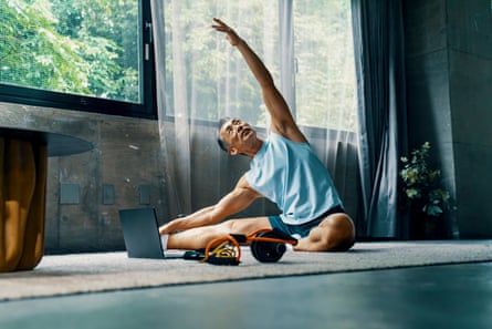 Senior male works out at home while watching a laptop computer in a modern interior home with window and view of nature in the background.