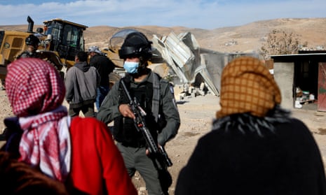 Palestinians gather in front of Israeli forces as an Israeli machinery demolishes a Palestinian structure in January 2022