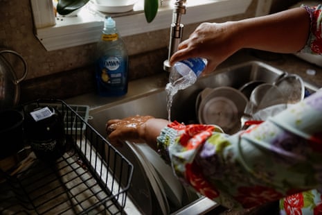 A person washes dishes using bottled water.