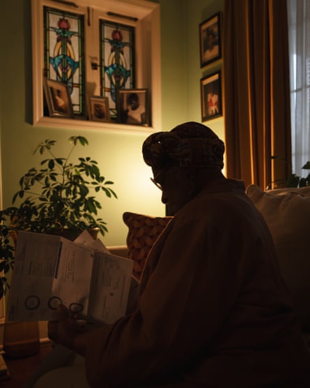a person silhouetted by a single light sorts through her utility bills in her living room where portraits of her family hang