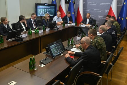 Donald Tusk and and a dozen others, some in military uniform, sit around a table, with Polish and EU flags in the background