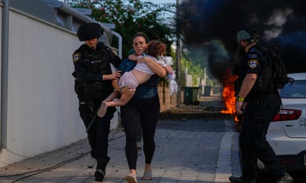 عناصر من الشرطة الإسرائيلية يقومون بإجلاء امرأة وطفل من موقع أصيب بصاروخ أطلق من قطاع غزة في عسقلان، جنوب إسرائيل.