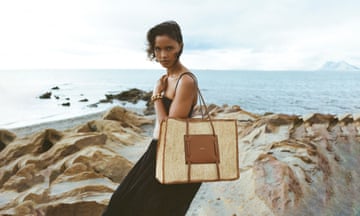 A female model holding a beige raffia bag on the beach