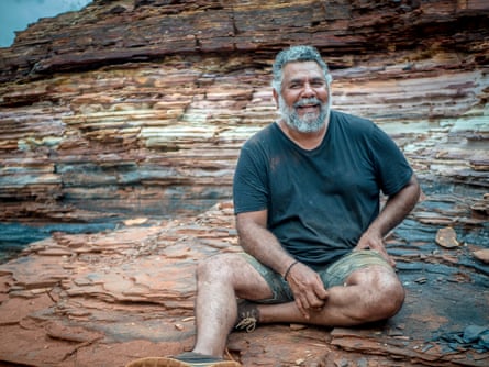 Michael Woodley est assis sur des rochers devant une falaise de pierre à bandes colorées