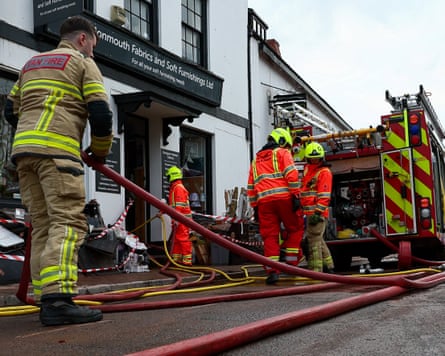 Four firefighters stand next to a fire engine and lay out hoses next to a flooded building