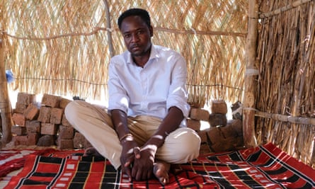 Sherif al-Deen, a social worker, sits in a grass hut on a red woven mat