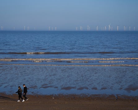 A beach on a windy day with wind turbines on the horizon.
