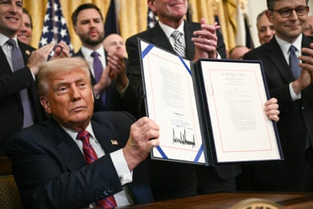 Trump holding a signed law with people applauding behind him