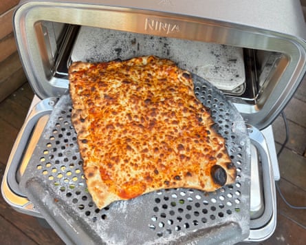 A cooked margherita pizza on a peel at the open door of a Ninja Artisan pizza oven.