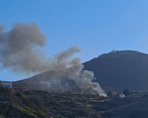 A plume of grey smoke rising from a hillside in to a clear blue sky with a mountain in the background qhxidiqxkiqrzinv