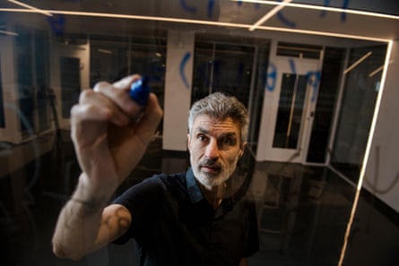 Middle-aged man writes in a pen on a pane of glass, photographed from behind the glass